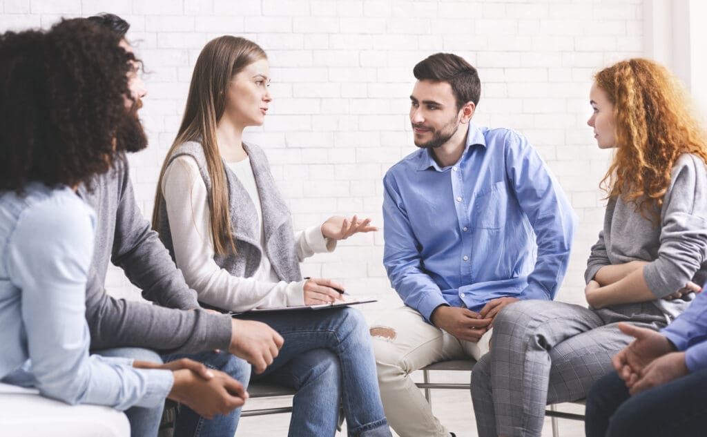 People sitting in circle and listening mentor during group therapy session