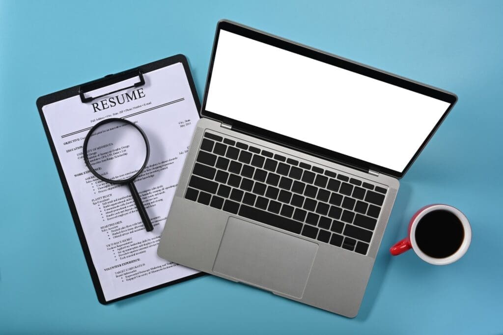 Above view laptop computer, magnifying glass and resumes applicants. Job search concept.