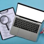 Above view laptop computer, magnifying glass and resumes applicants. Job search concept.
