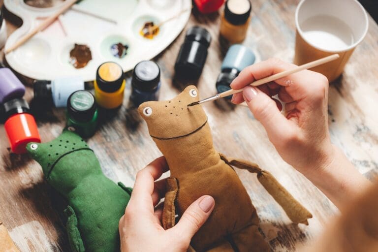 Handmade soft Doll frog. DIY gift making. Human hands hold frog soft toy.