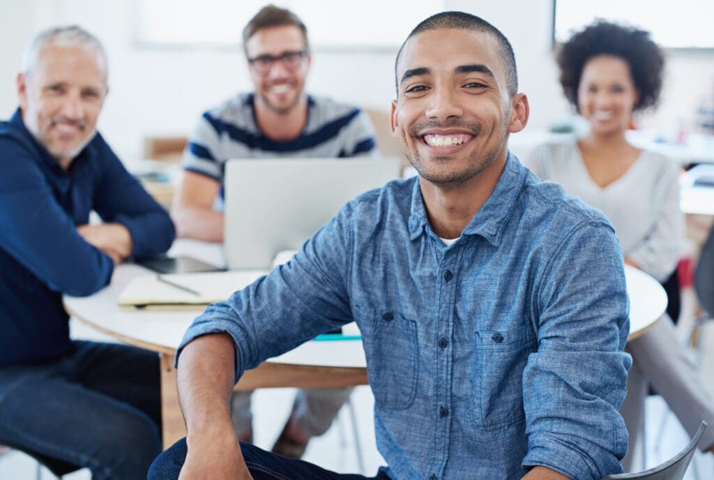 Portrait of a young office worker sitting at a table with colleagues in the background
