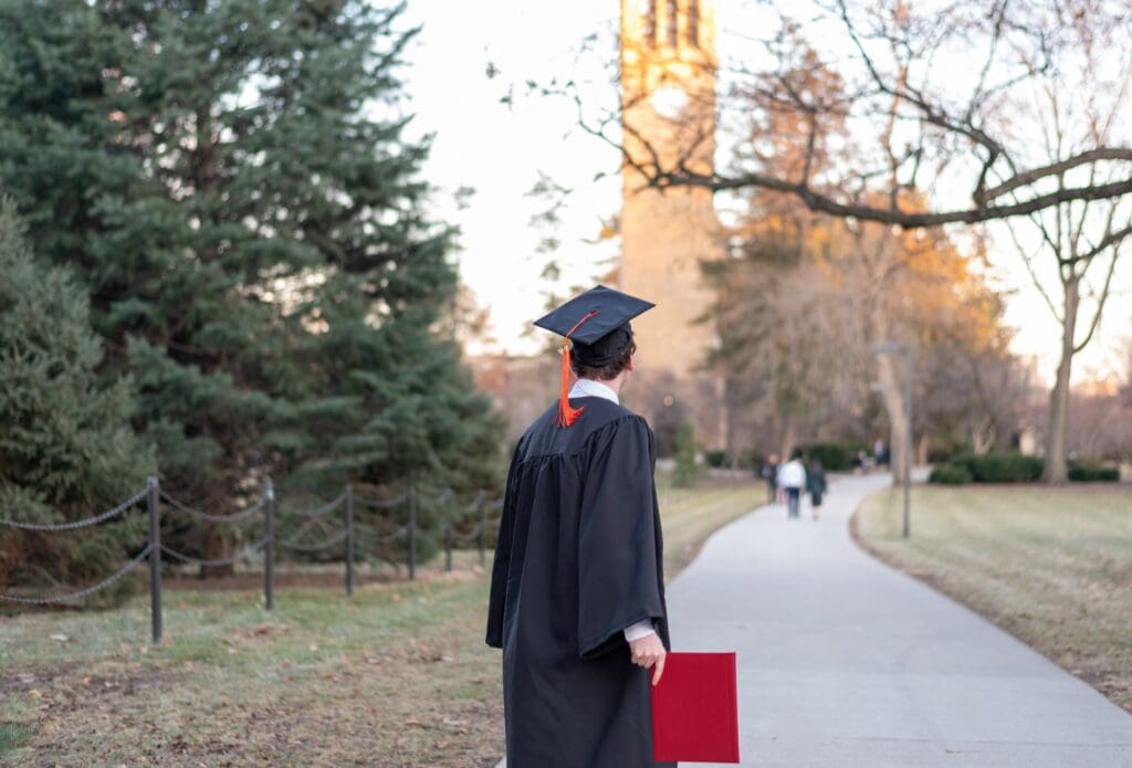 Back view of college graduate in cap and gown holding his diploma Leader Lab