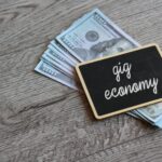 Chalkboard with text GIG ECONOMY on top of money with copy space.