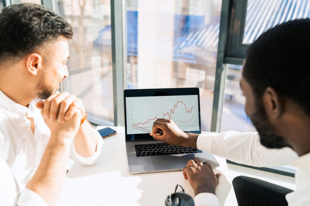 Two multiracial businessmen on laptop looking at company growth chart