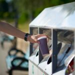 Man throwing paper coffee cup in waste sorting bin of the park