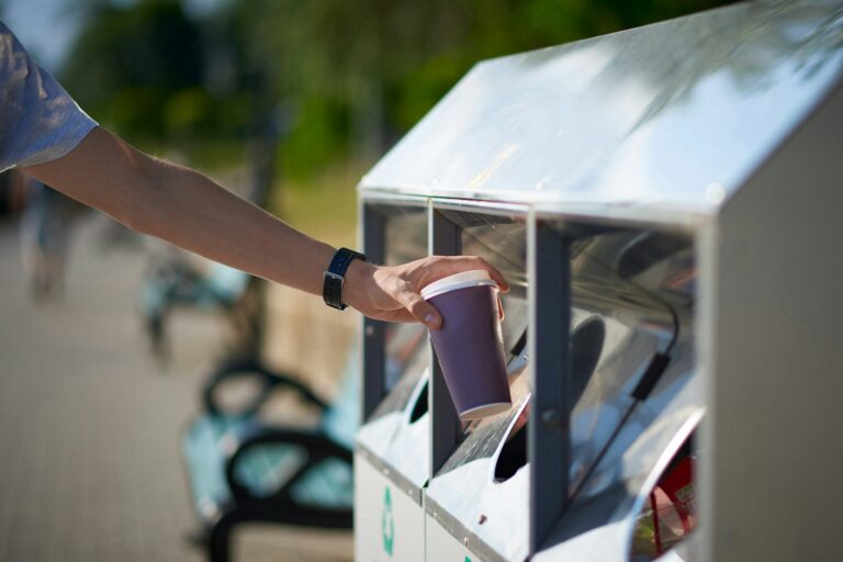 Man throwing paper coffee cup in waste sorting bin of the park