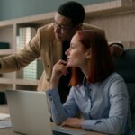 African American male mentor teaching Caucasian female employee explain online software marketing
