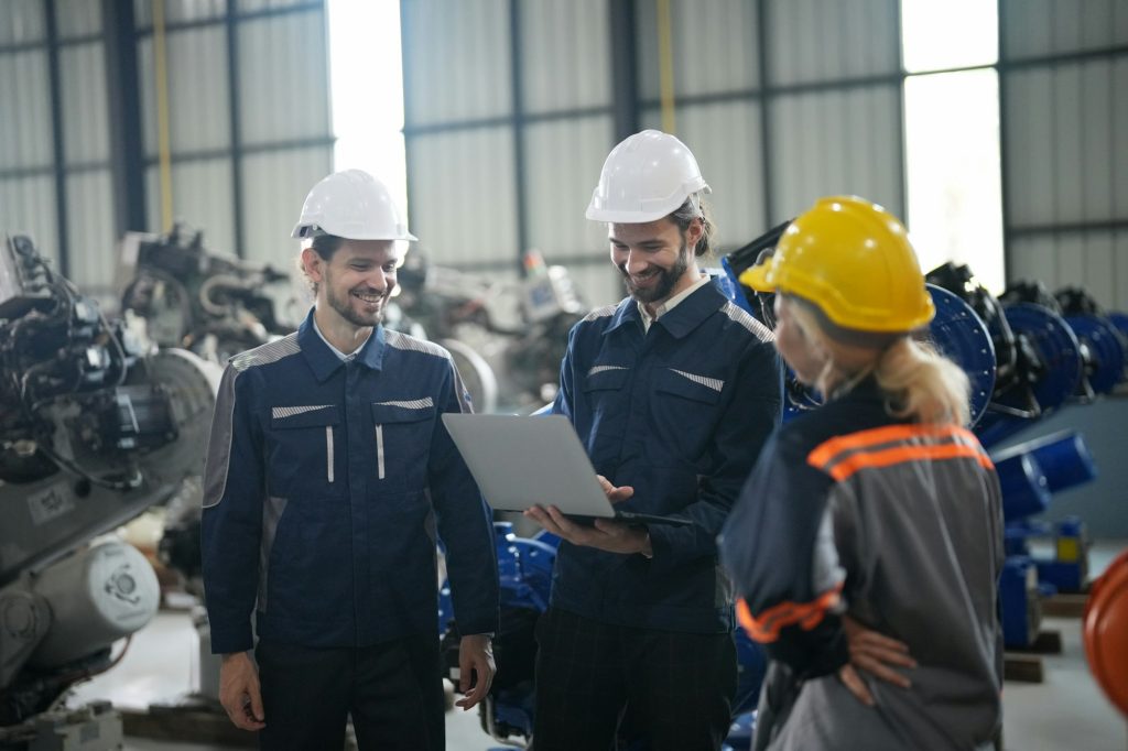 Engineer explaining to controlling robotic welding process to welder in factory.