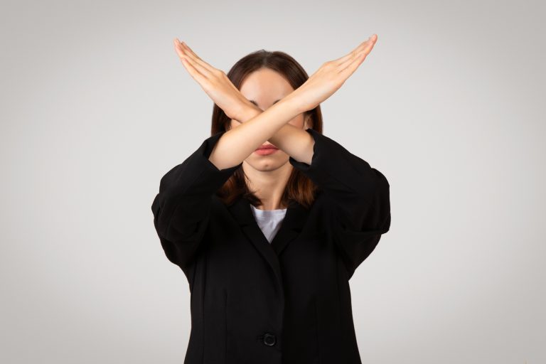 Businesswoman with her eyes covered by crossed hands making an X sign, symbolizing rejection