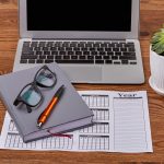 Top view business calendar with laptop and glasses on wooden desk.