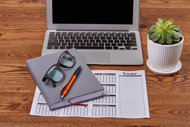 Top view business calendar with laptop and glasses on wooden desk.