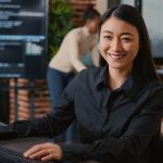 Asian software developer smiling and resuming work typing code on computer keyboard