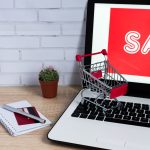 E-commerce concept. Laptop with red inscription ant toy trolley on wooden table