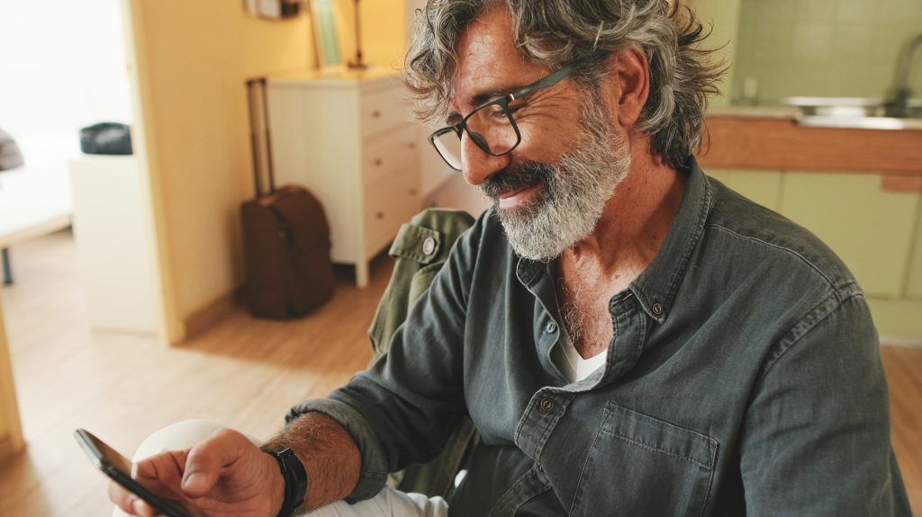 Close-up of an elderly man attentively reading message on his smartphone and drinking coffee