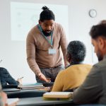 Teacher talking to senior man during adult education training class in lecture hall.