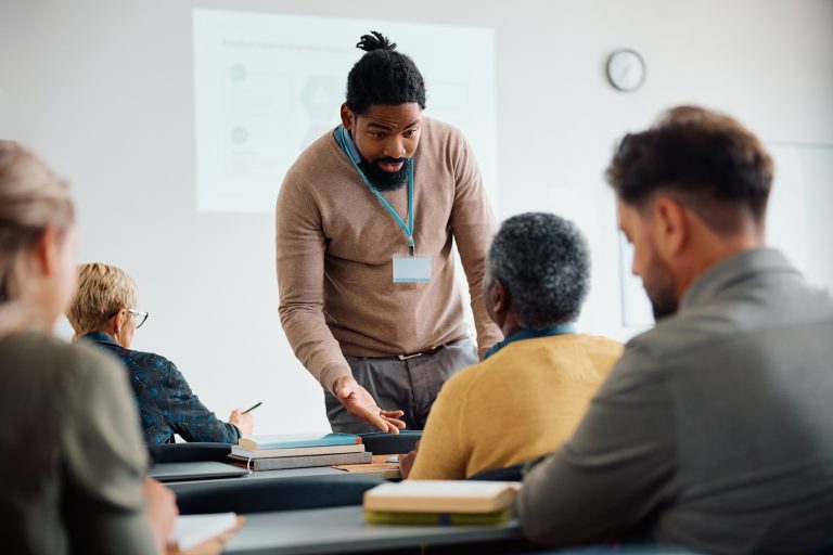 Teacher talking to senior man during adult education training class in lecture hall.