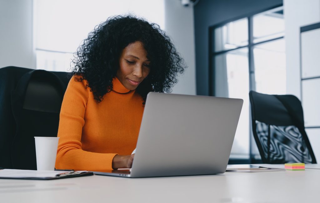Concentrated professional woman in a bright orange top engages with laptop in a modern office