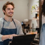 Smiling helpful young waiter servicing the customer at cash point in cafe