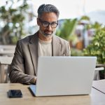 Busy mature business man executive sitting at outdoor table using laptop.