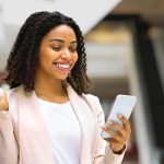 Discount App. Smiling Woman With Shopping Bags Using Smartphone In Mall